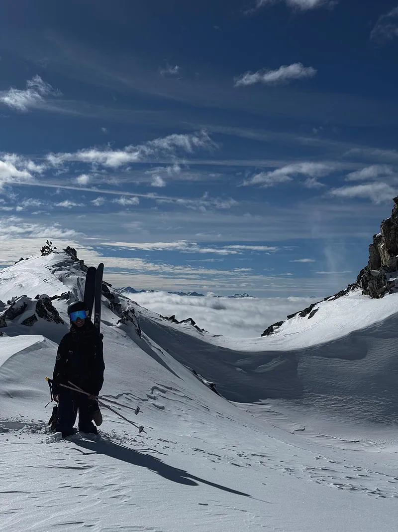 Valentina on the ridge, skis on her shoulder, above the clouds